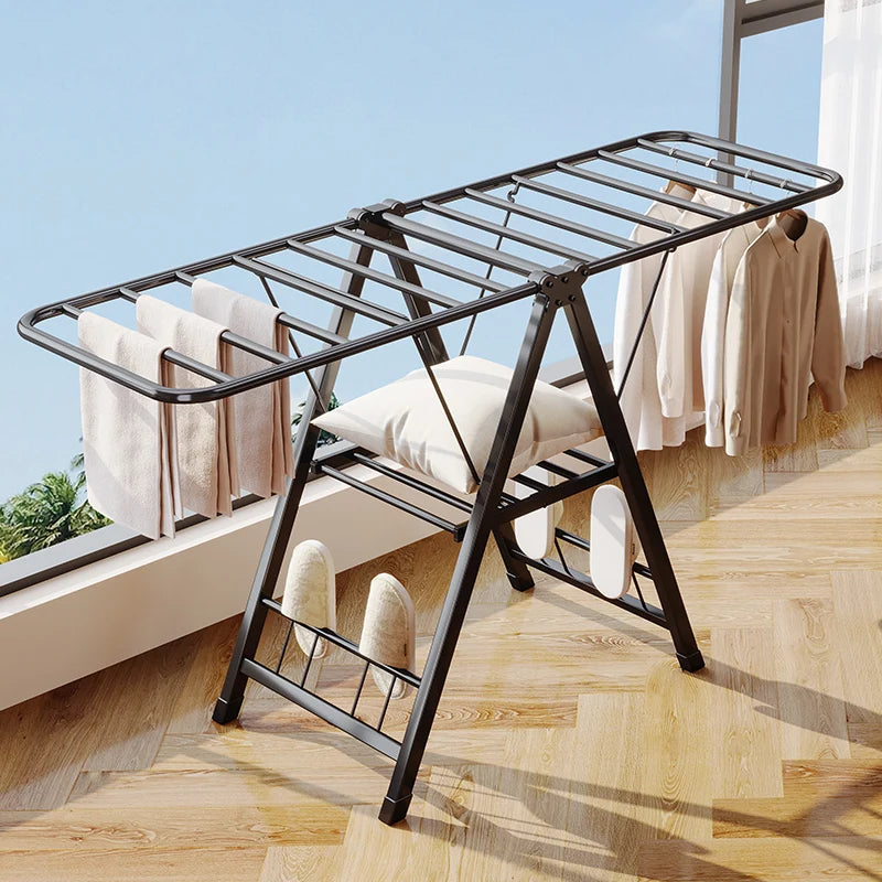 Clothing drying rack with clothes on a wooden floor next to a window with curtains.