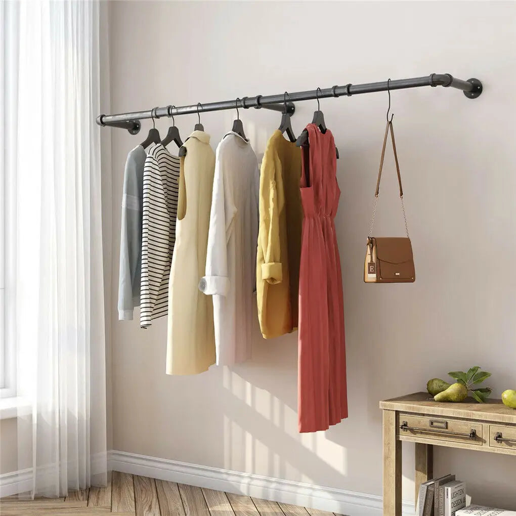 Clothing rack with various garments and a handbag against a neutral wall.