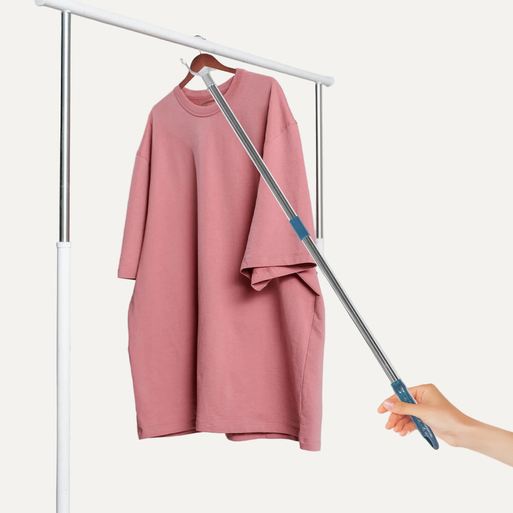 Pink dress on a hanger with a telescopic rod held by a hand against a light gray background