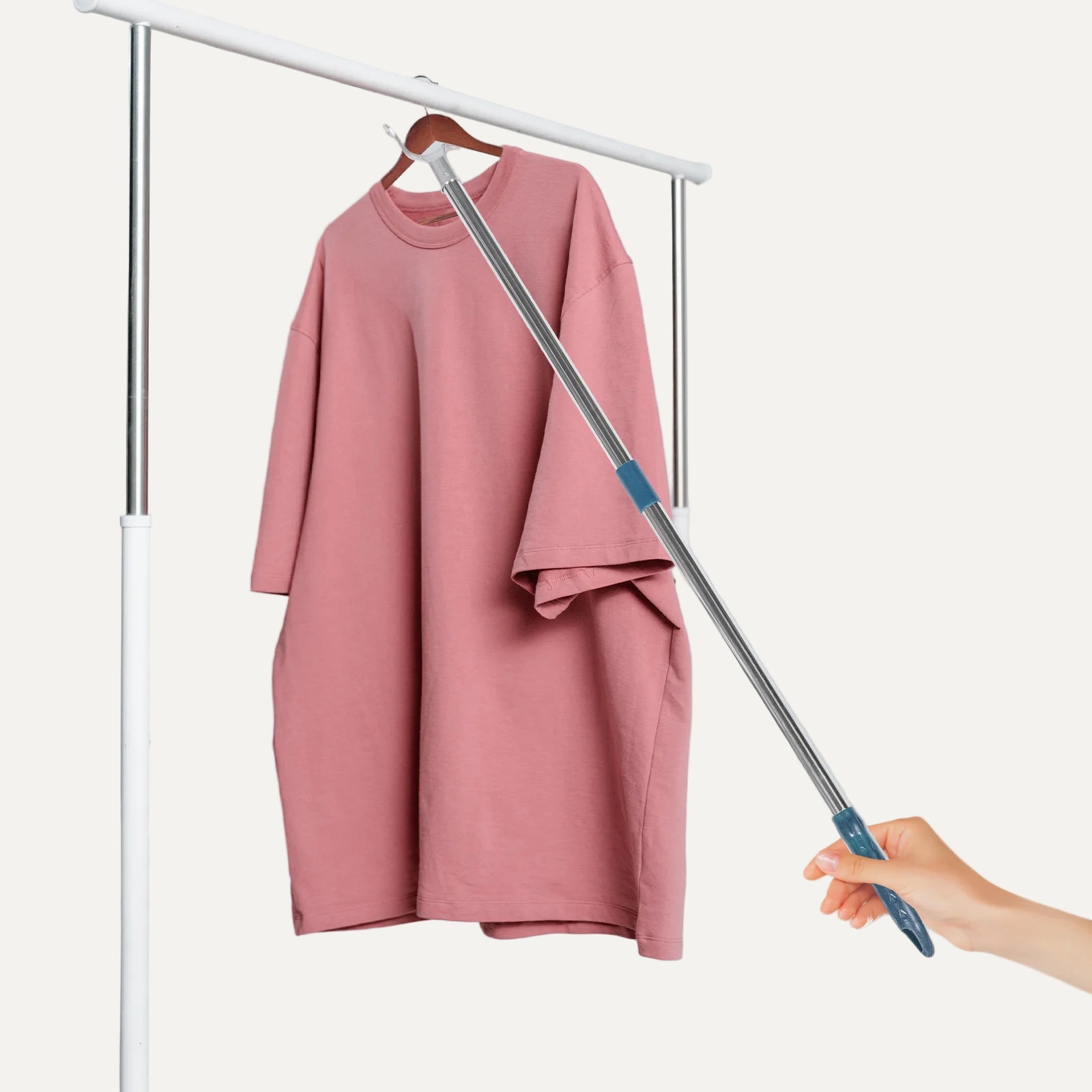 Pink dress on a hanger with a telescopic rod held by a hand against a light gray background