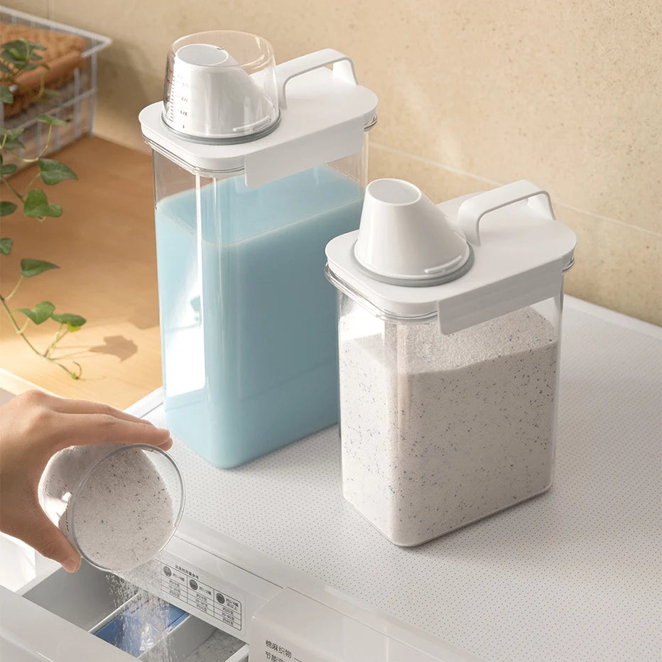 Two detergent storage containers on a counter with a hand pouring detergent powder into a washing machine.