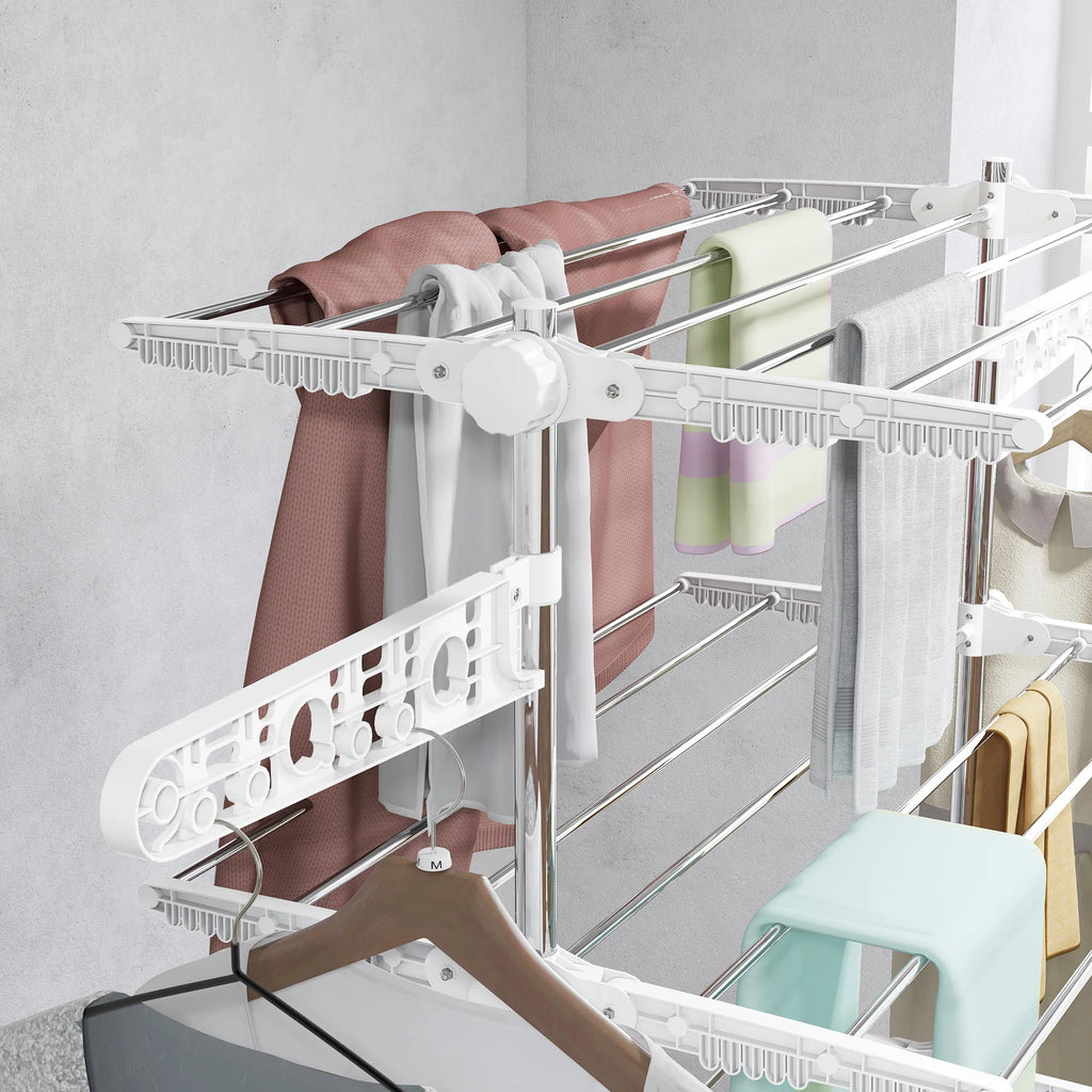 White clothes dryer rack with folded clothes against a light gray wall.